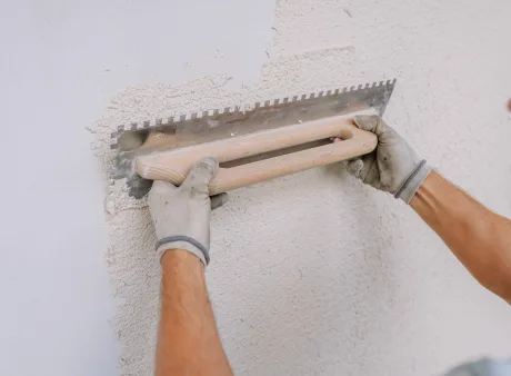 Ein Arbeiter glättet Gips an einer Wand mit einer gekerbten Kelle mit Kalkputz.